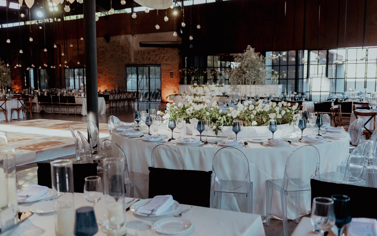 The same hall built out: long tables under the arched window, hanging lights and low floral runners.