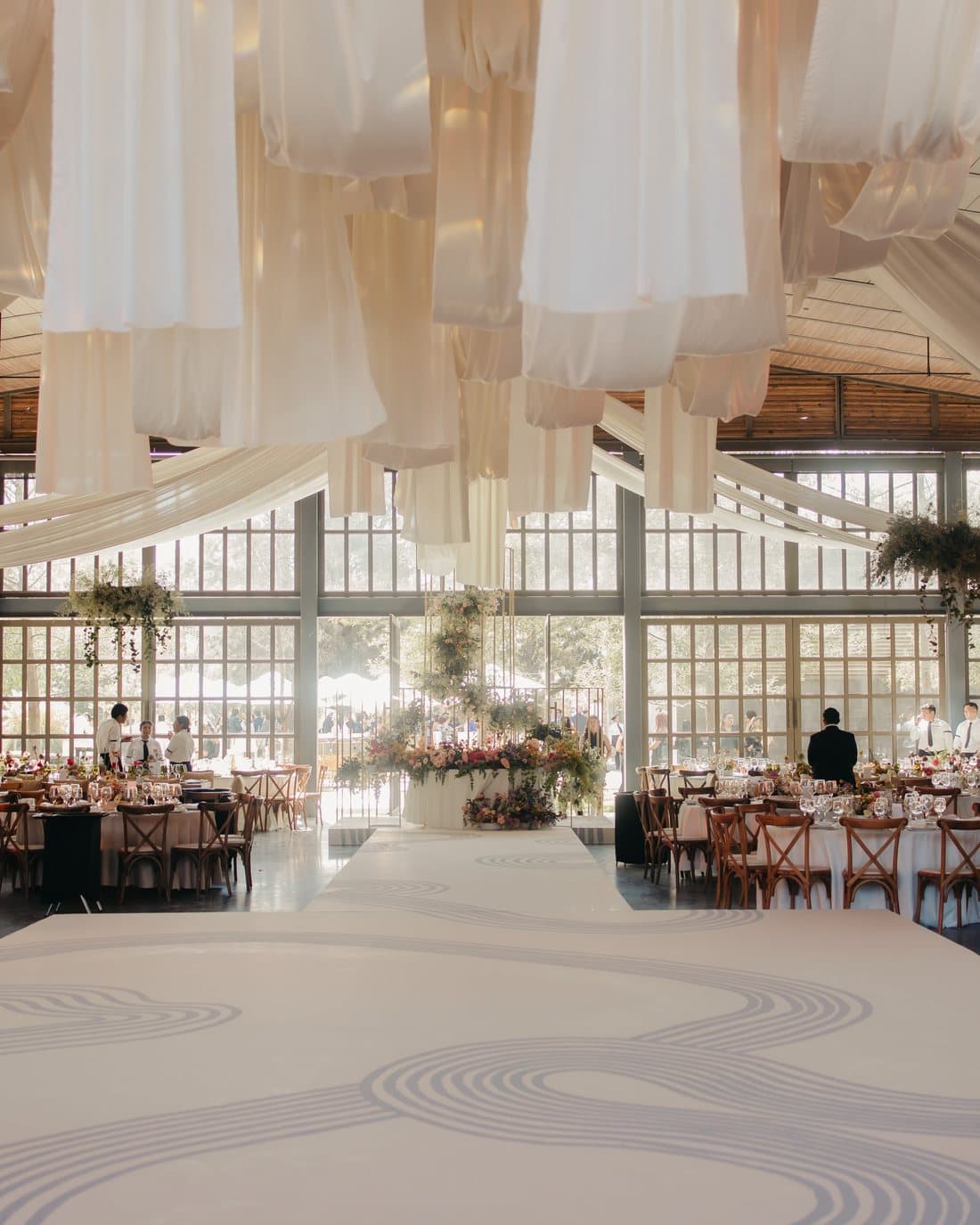An empty ballroom with fabric draped across the ceiling and a patterned dance floor, set and waiting.