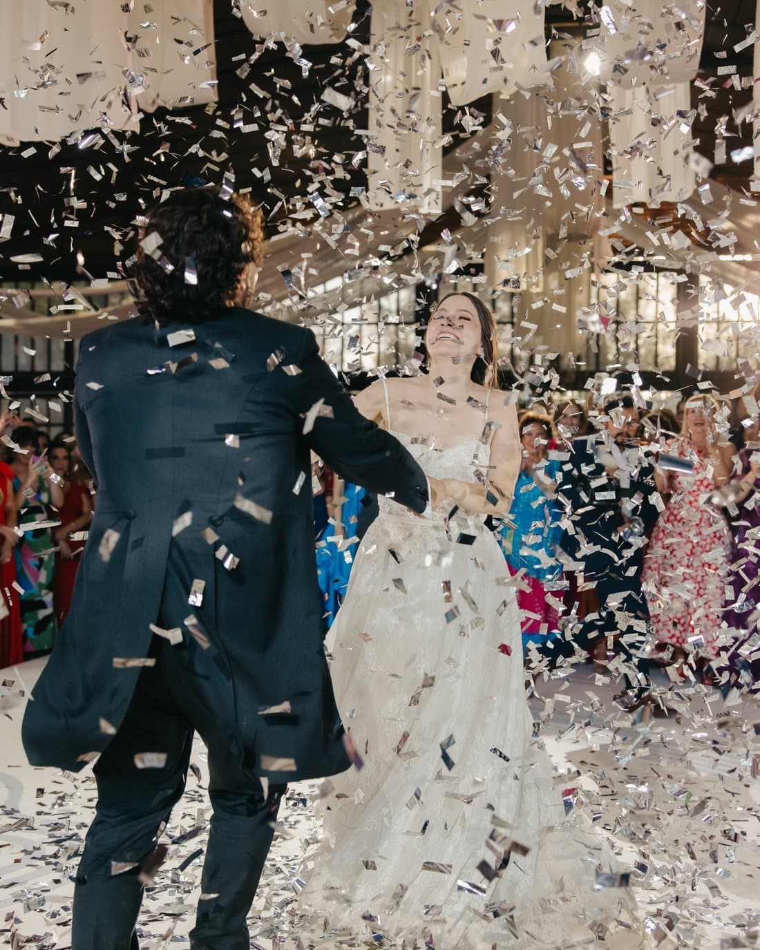 A couple crossing a room in a dense fall of confetti as the celebration begins.