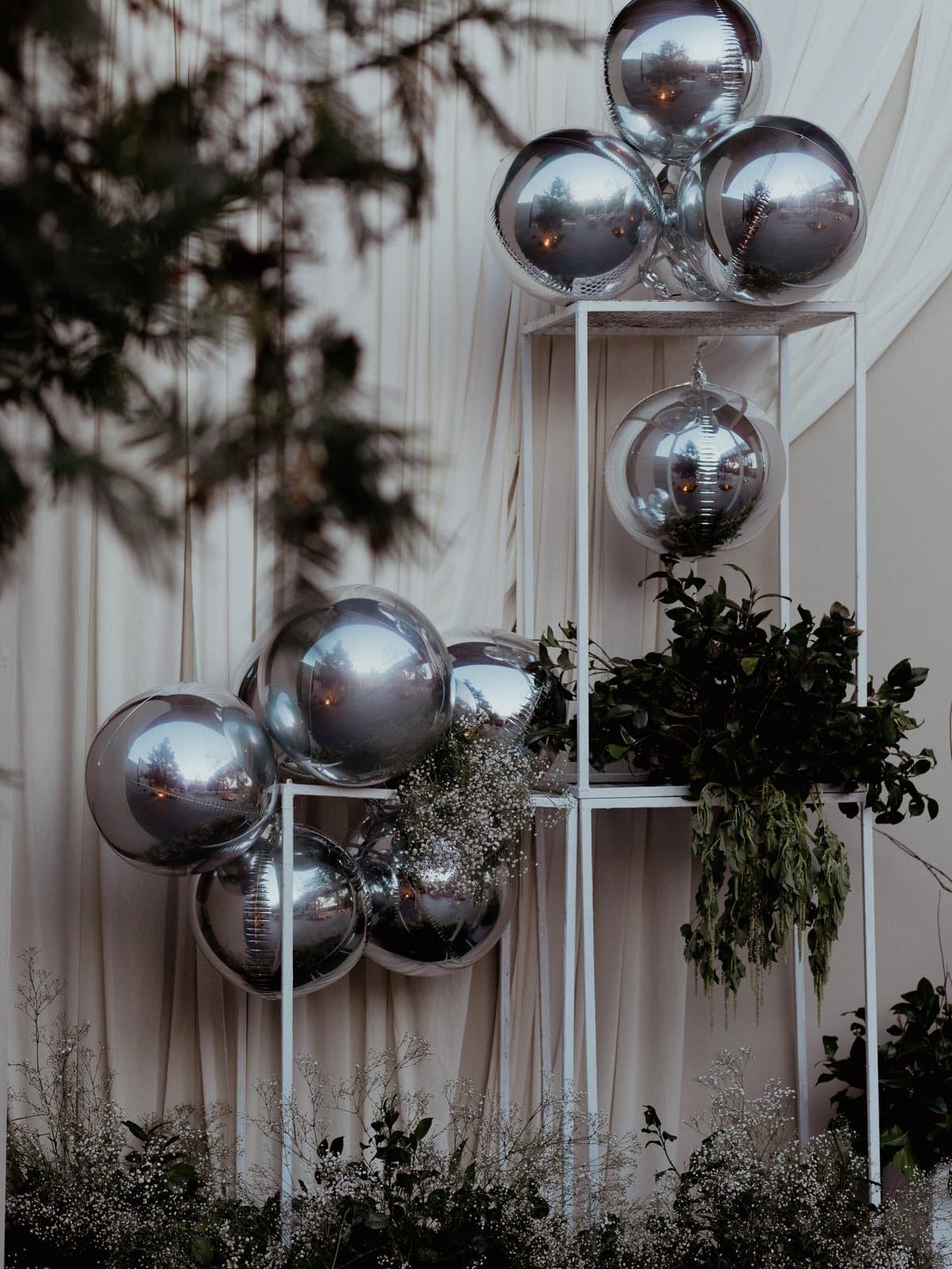 A sculptural installation of mirrored spheres on white plinths, framed by dark foliage.