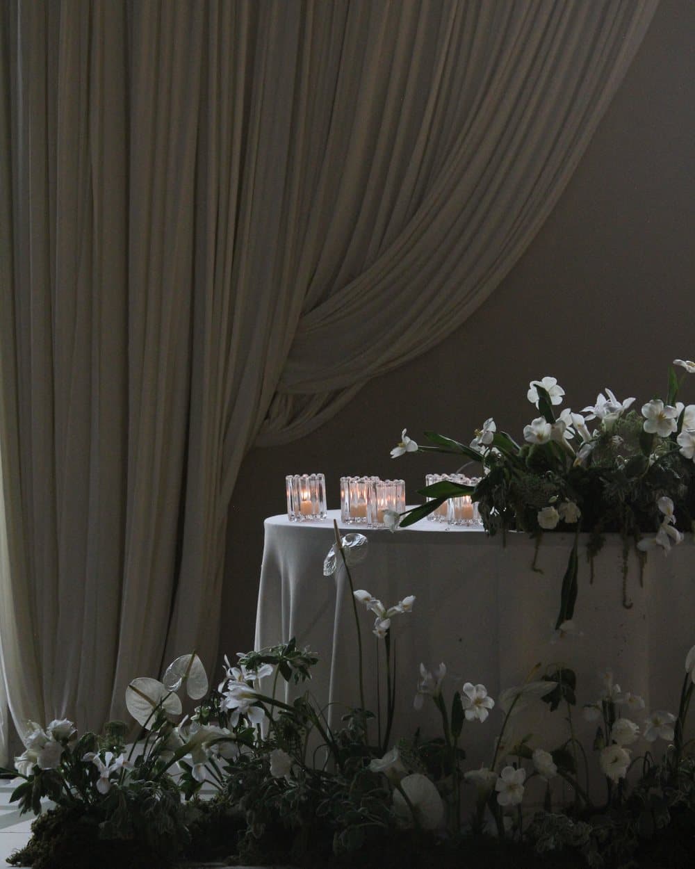 White orchids and candles along a draped table edge in low, diffused light.