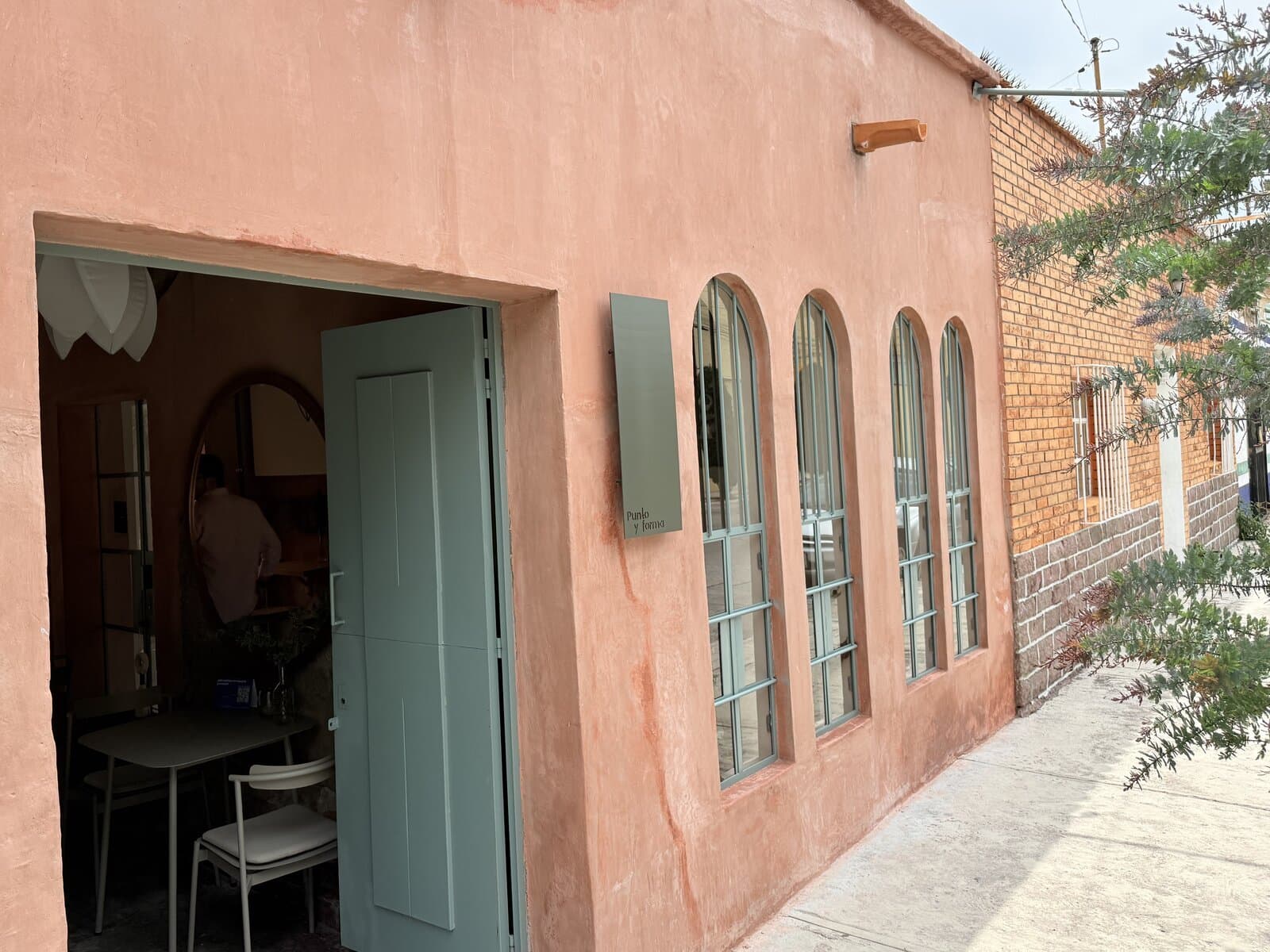 Fachada de Melchor en terracota, con la puerta verde abierta y la placa de Punto y Forma junto a las ventanas en arco.