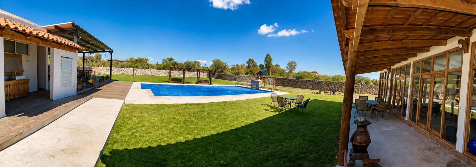Vista panorámica de Villa Alvento: portal cubierto, jardín, alberca y el muro de piedra que cierra la propiedad.